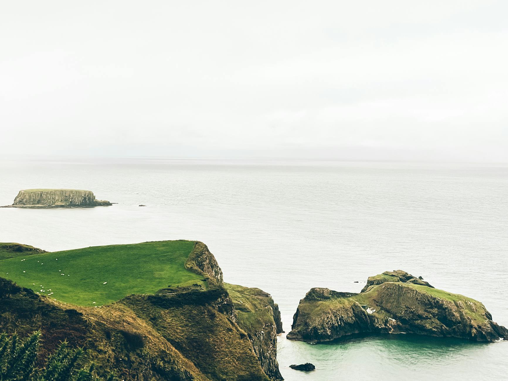 Rugged green coastal cliffs meeting the Atlantic Ocean at Ballycastle, Northern Ireland, under soft overcast skies along a British Isles cruise route from Bilbao.