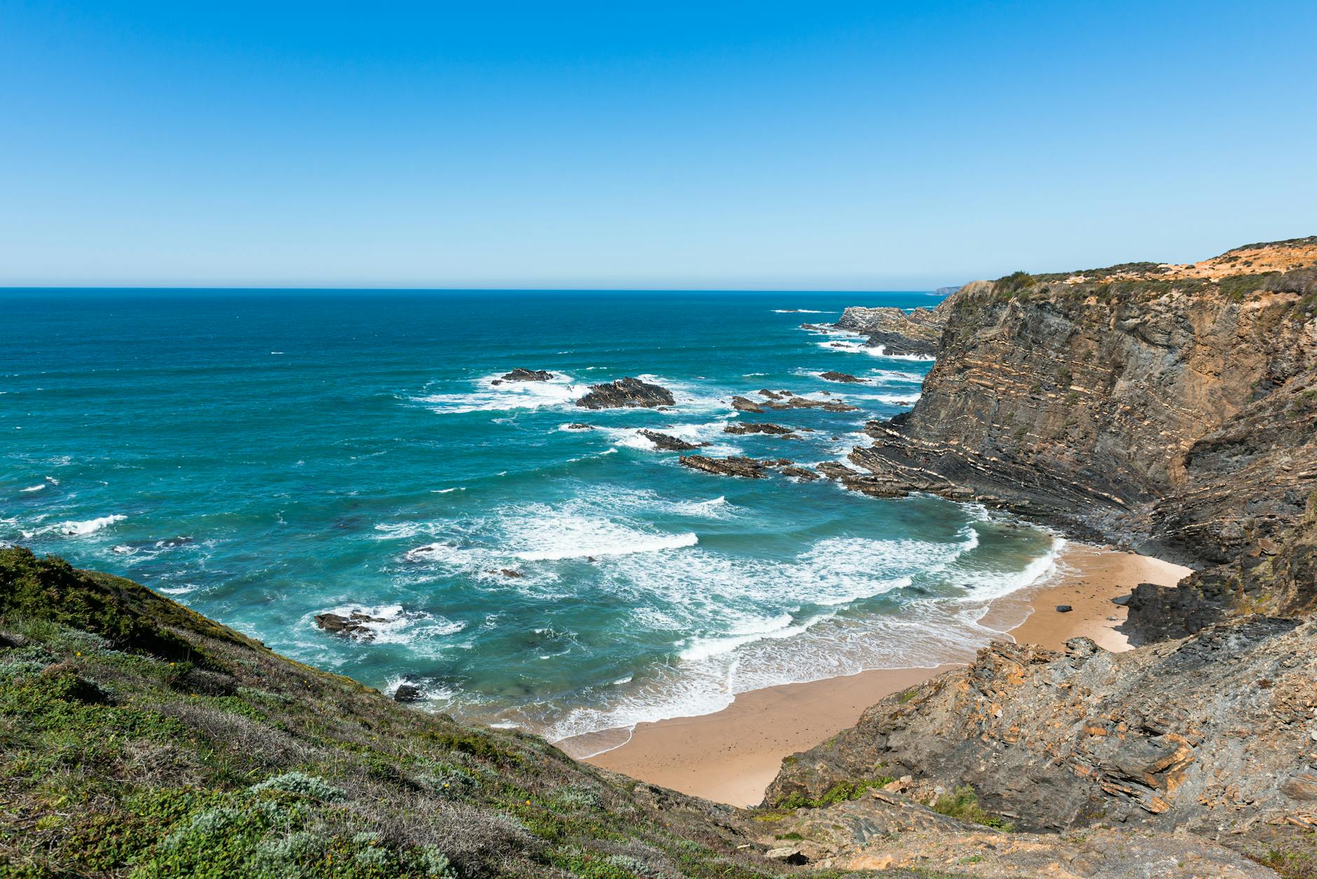 Dramatic golden cliffs of Portugal's Alentejo coast rising above the deep blue Atlantic Ocean, capturing the raw beauty of Europe's western seaboard along the cruise route.