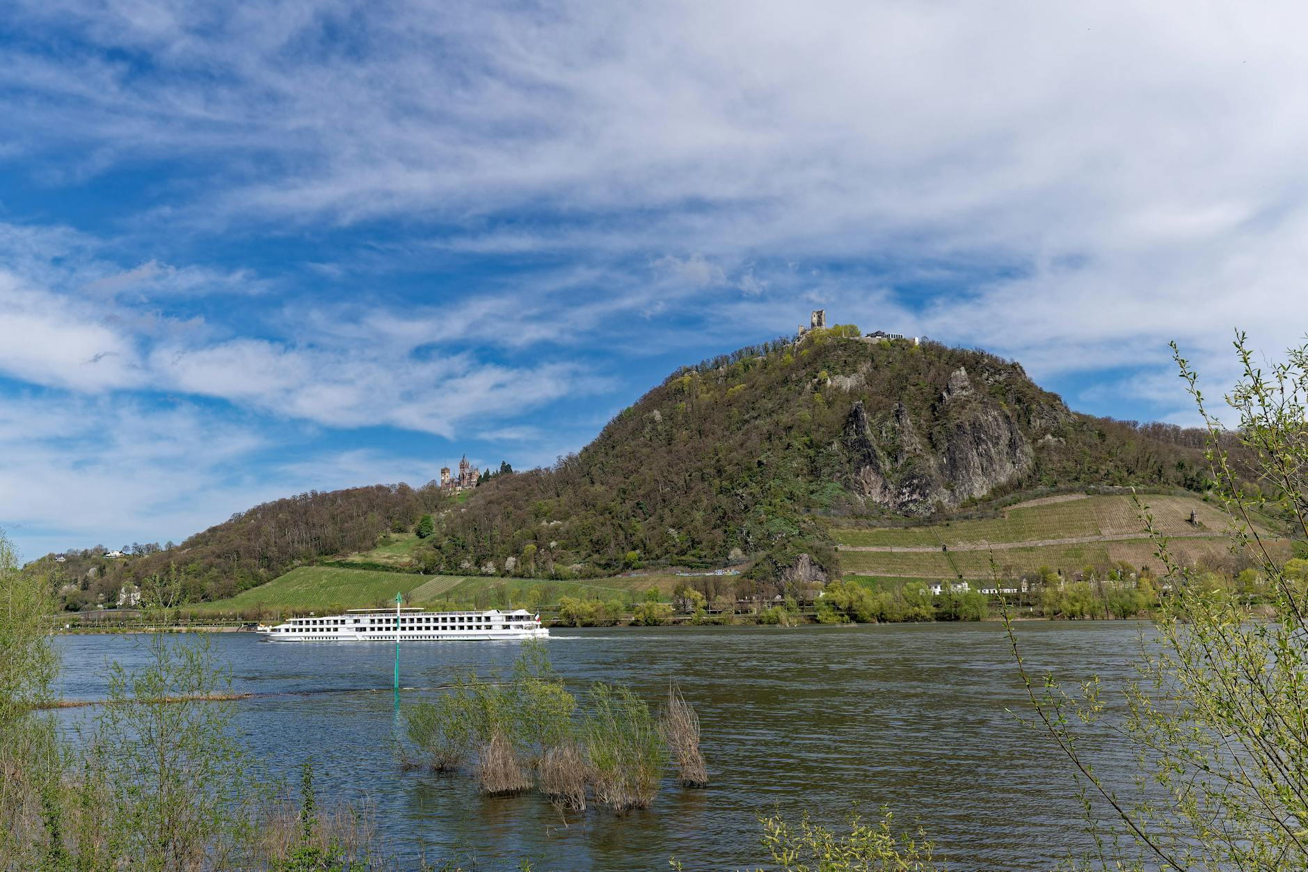 A river cruise ship glides along the Rhine River beneath a castle-topped hillside, capturing the scenic charm of European river cruising.