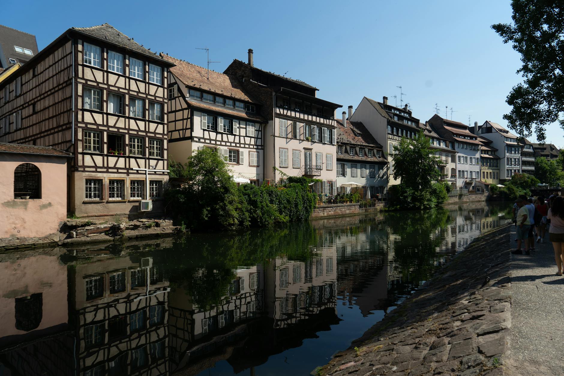 Strasbourg's iconic half-timbered houses reflecting in the calm waters of the Ill River under a clear blue sky, a quintessential European riverside destination on Basel cruise itineraries.