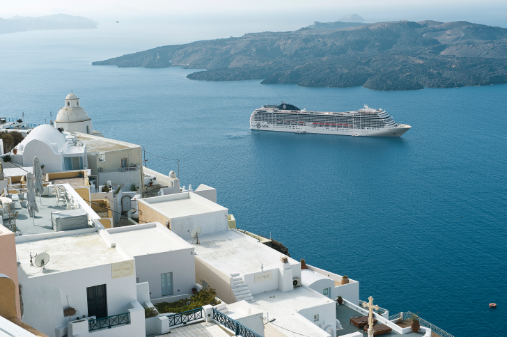 MSC Musica aerial view sailing near Santorini with whitewashed buildings cascading down volcanic cliffs and deep blue Aegean Sea.