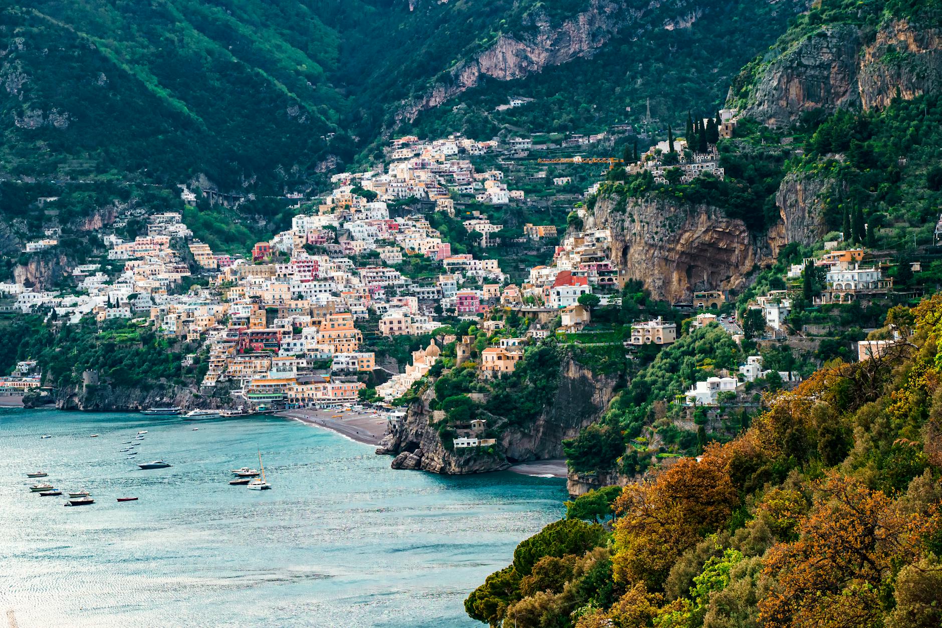Pastel-colored houses of Positano cascading down steep Mediterranean cliffs to the turquoise sea below, capturing the iconic Amalfi Coast scenery along a classic cruise route