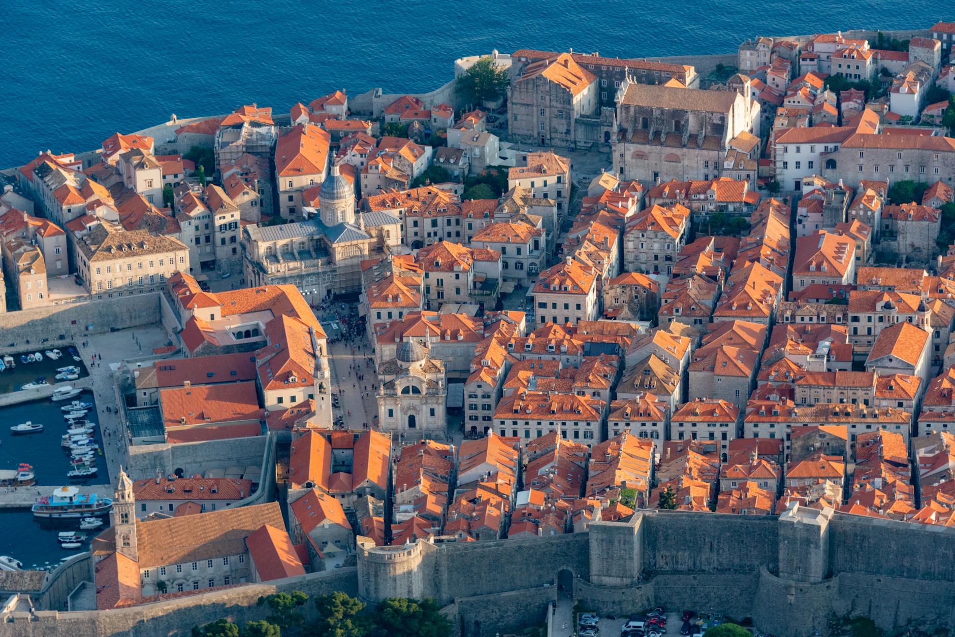 Aerial view of Dubrovnik's Old Town with terracotta rooftops and ancient stone walls extending along the deep blue Adriatic Sea coastline, a signature port of call on Mediterranean cruise itineraries.