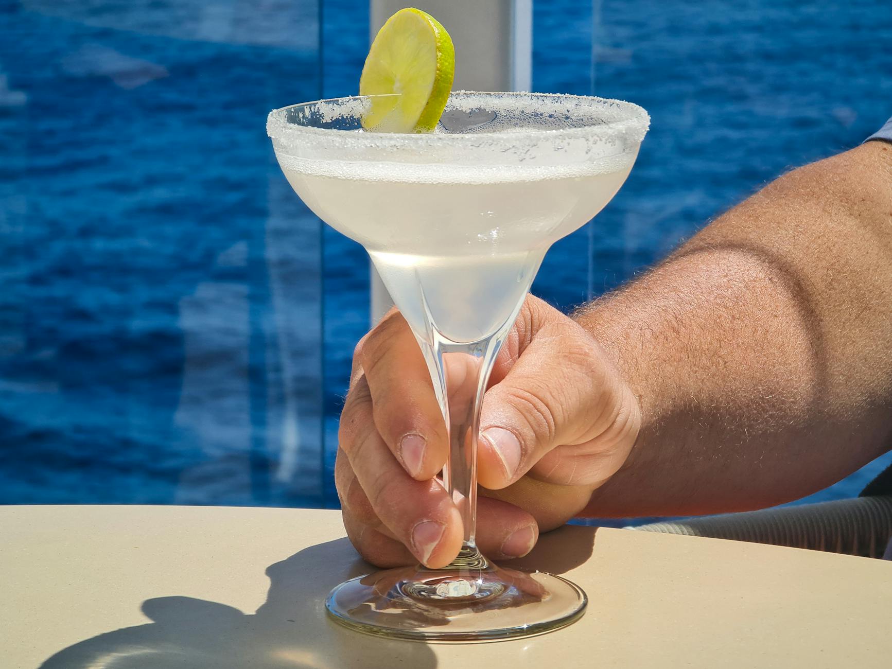 A refreshing margarita cocktail garnished with lime served on a cruise ship deck, evoking the tropical bar experience of Harmony of the Seas' amplified Lime & Coconut venue.