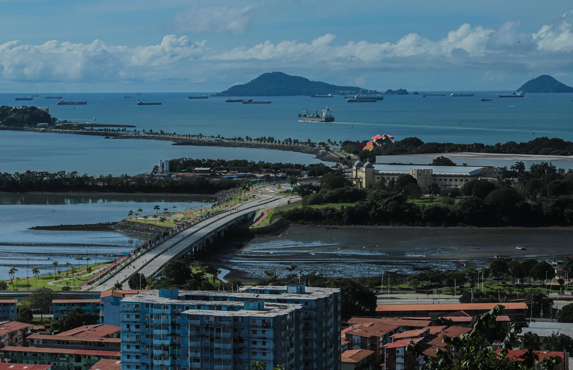Aerial view of ships in Panamá Bay, featuring lush islands and urban landscape under a clear sky.