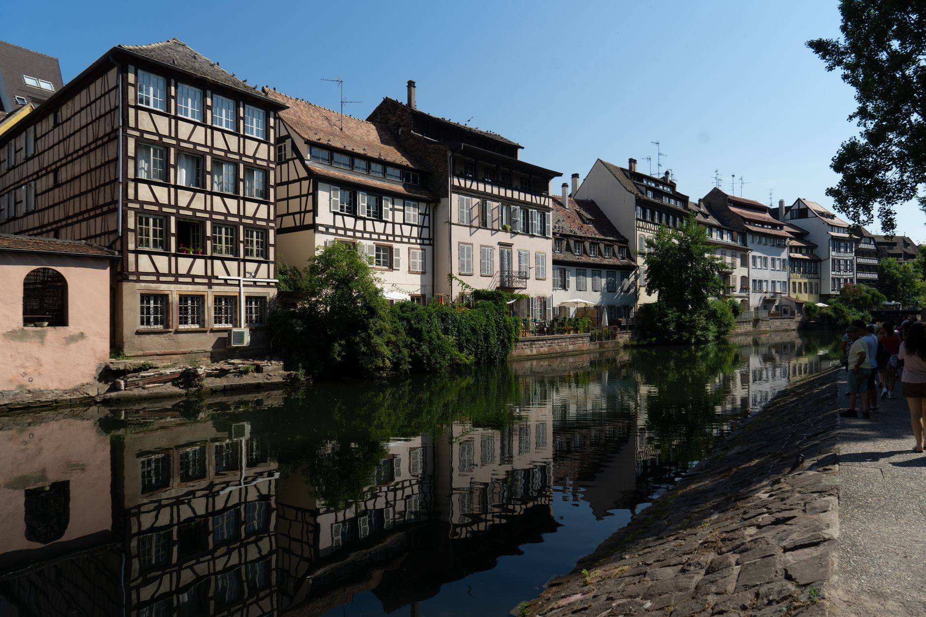 Strasbourg's iconic half-timbered houses reflecting in the calm waters of the Ill River under a clear blue sky, a quintessential European riverside destination on Basel cruise itineraries.