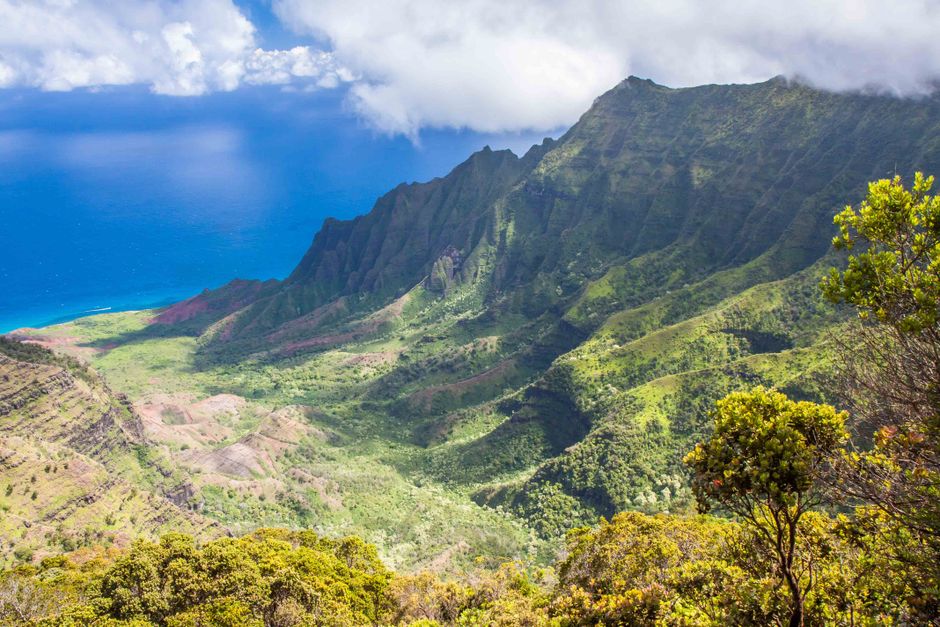 The lush green cliffs of Kauai's Na Pali Coast rise dramatically above the blue Pacific Ocean, as seen from sea level
