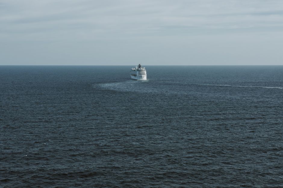 A lone cruise ship traversing the vast open Pacific Ocean near Australia under a clear sky, evoking the scale of a transpacific voyage from Auckland to Hawaii.