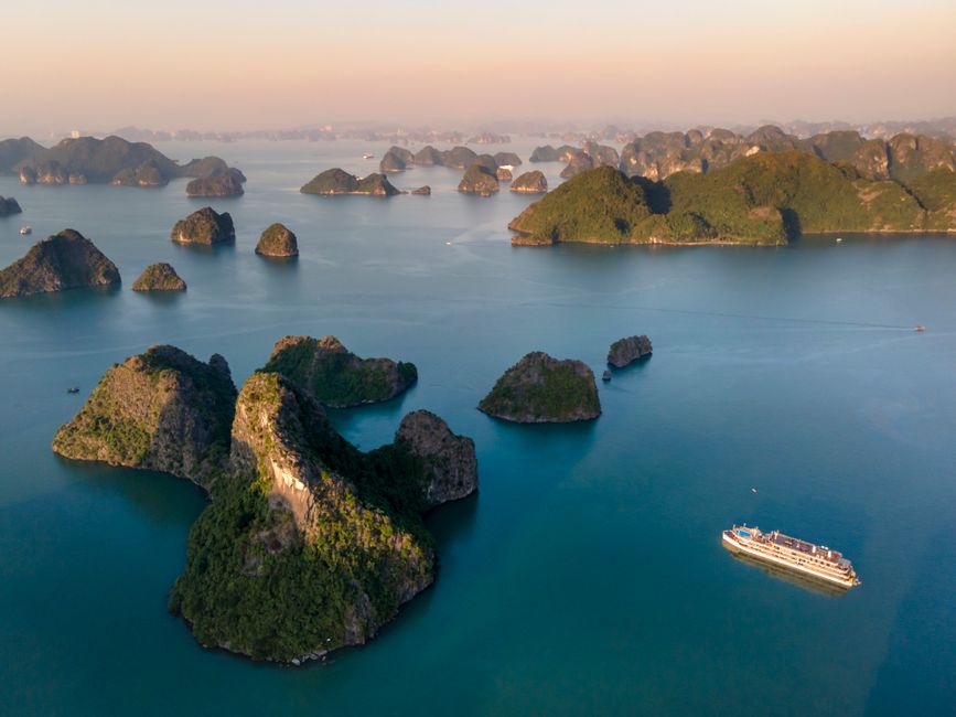 Stunning aerial view of Ha Long Bay's limestone karsts and cruise ship during sunrise.