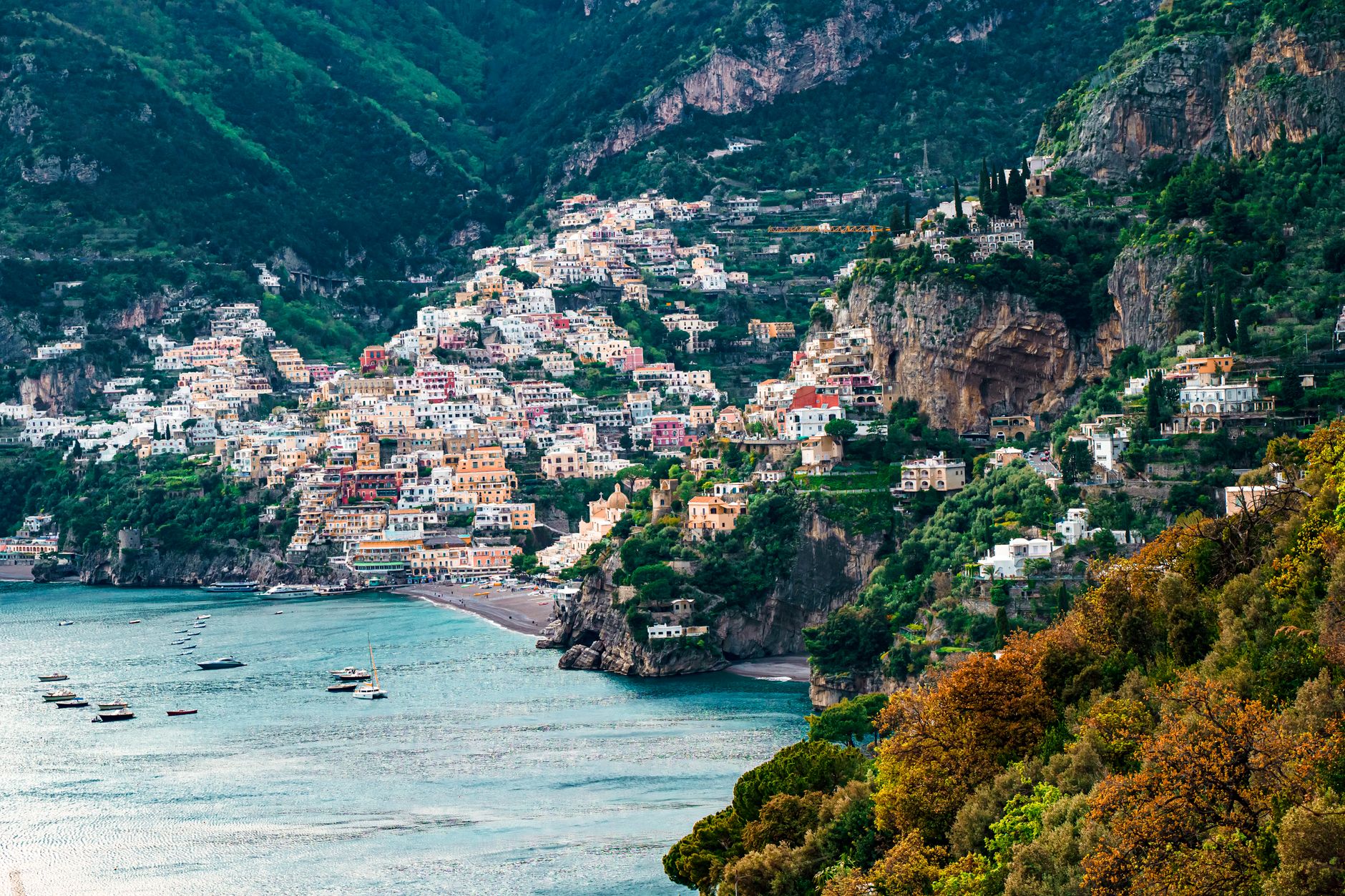 Pastel-colored houses of Positano cascading down steep Mediterranean cliffs to the turquoise sea below, capturing the iconic Amalfi Coast scenery along a classic cruise route
