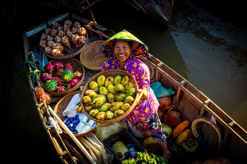 A joyful woman selling fresh fruits from her boat on a sunny day at a floating market.