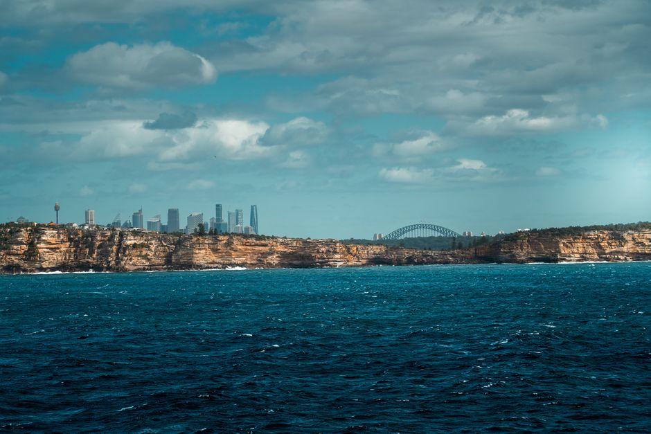 Dramatic coastal cliffs with the Sydney skyline and Harbour Bridge in the background.