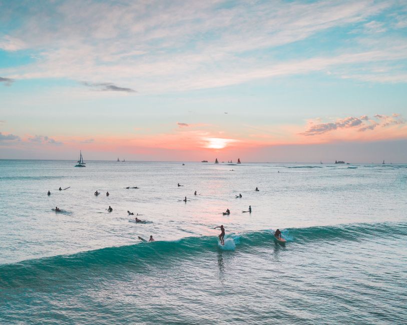 A picturesque scene of surfers riding waves at sunset on a tropical beach, with a vibrant sky creating a serene atmosphere.