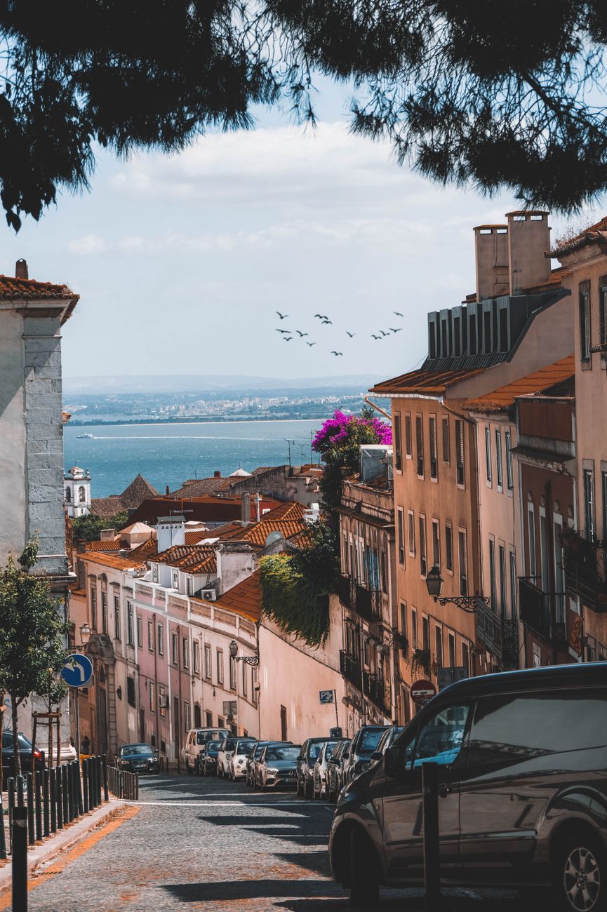 Scenic Lisbon street with ocean view, colorful buildings, and cars on a sunny day.