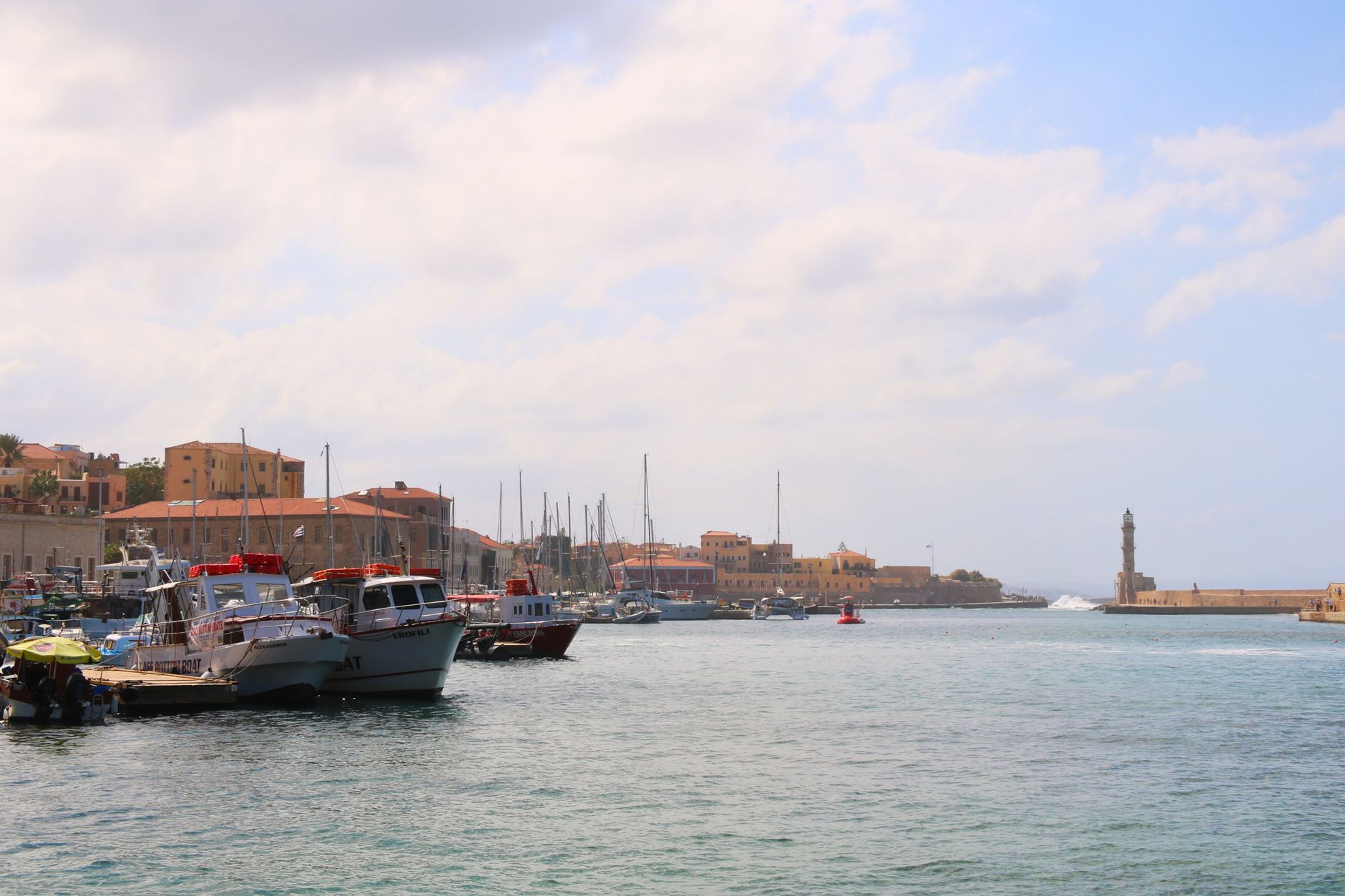 Chania's Venetian harbor featuring historic stone architecture and traditional boats moored along the waterfront under warm, bright Mediterranean sunlight