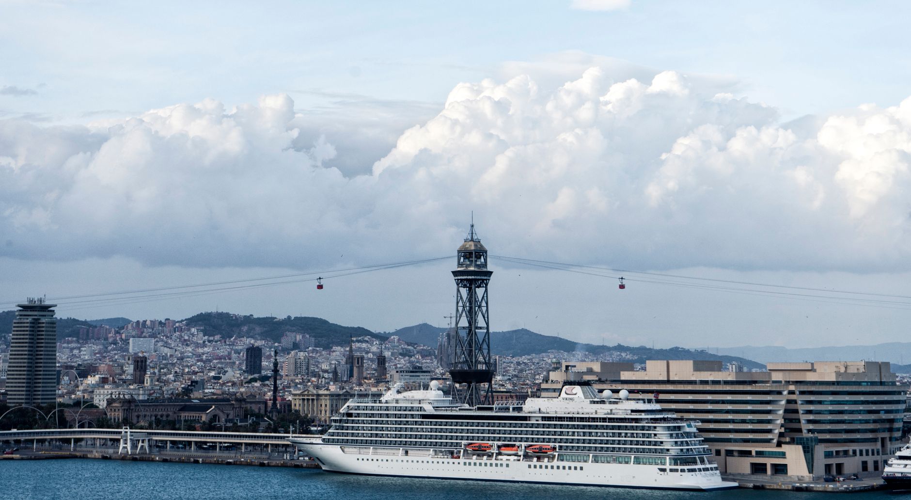 Barcelona harbor on embarkation day, with a cruise ship docked against the city skyline under dramatic Mediterranean skies