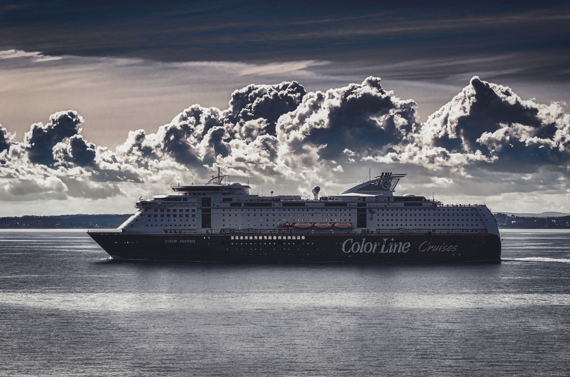 A cruise ship crossing the open ocean under dramatic billowing clouds, evoking the grandeur of a transatlantic voyage.