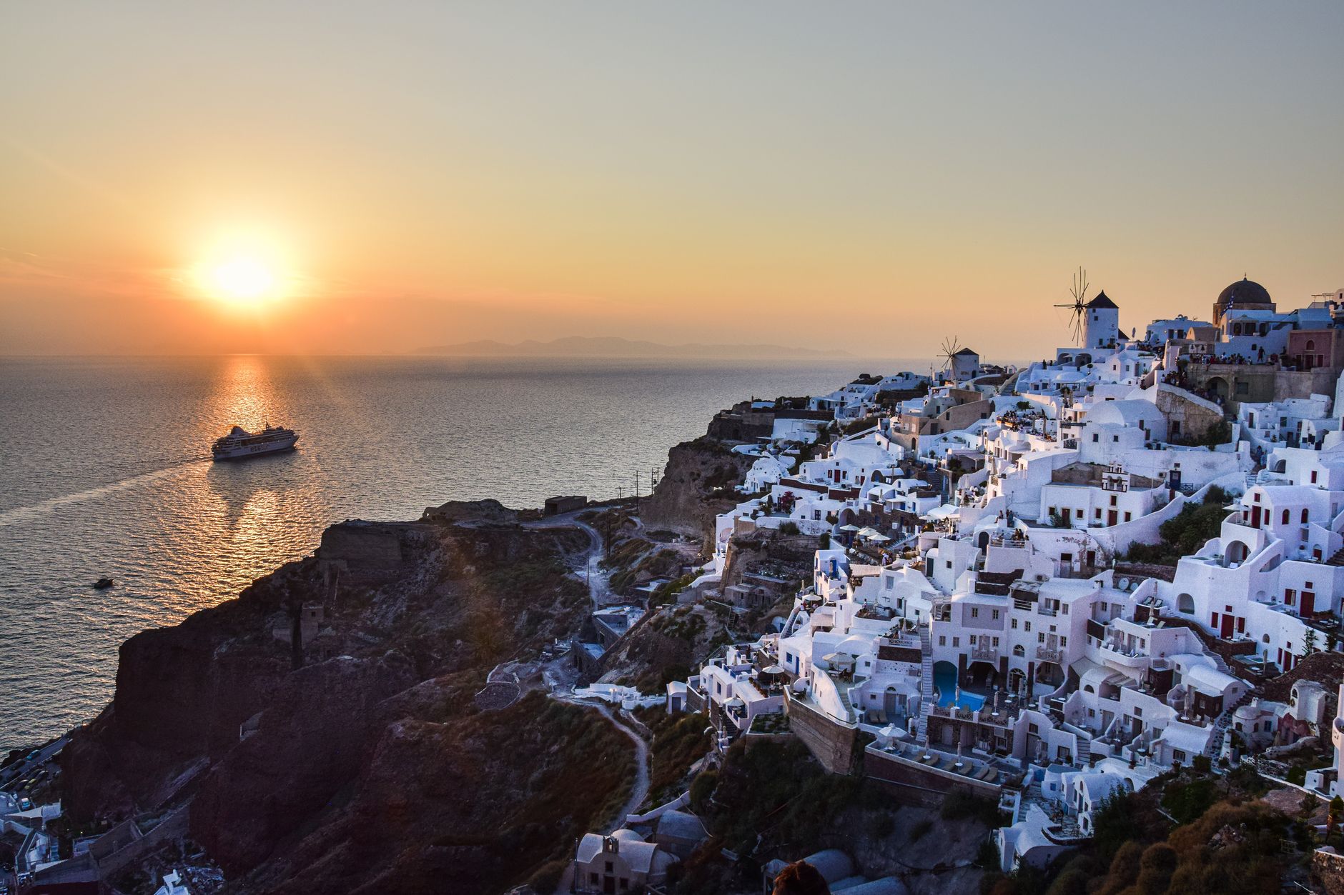 Santorini's iconic whitewashed buildings cascade toward the Aegean Sea as a cruise ship anchors offshore, illustrating the Eastern Mediterranean destinations shaping Celebrity Cruises' forward itinerary.