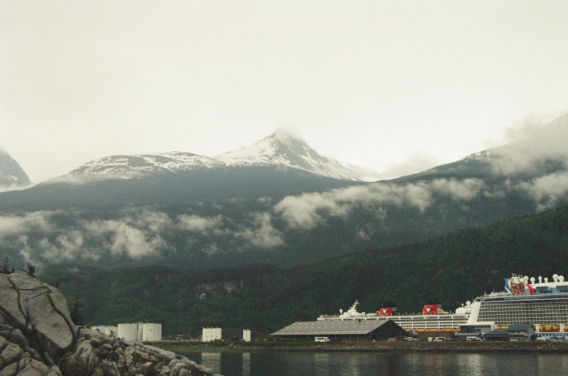 A cruise ship docked in Skagway, Alaska's harbor with snow-capped mountains rising behind the port town, illustrating a typical Inside Passage destination call.