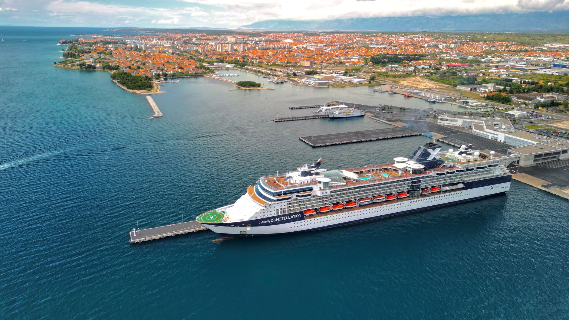 Explore a stunning aerial shot of a cruise ship at a bustling harbor with a vibrant coastal city backdrop.
