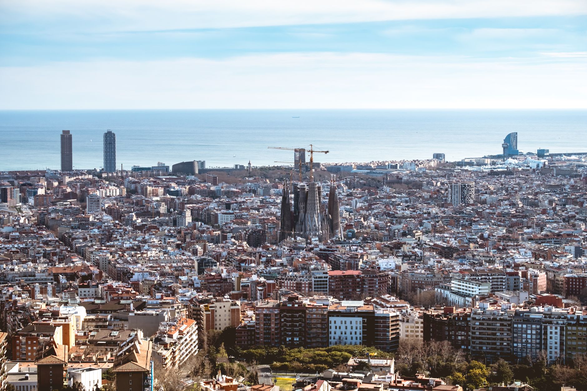 Aerial view of Barcelona's sun-drenched skyline with the Sagrada Familia rising above terracotta rooftops along the Mediterranean coastline, a premier Western Mediterranean cruise port.