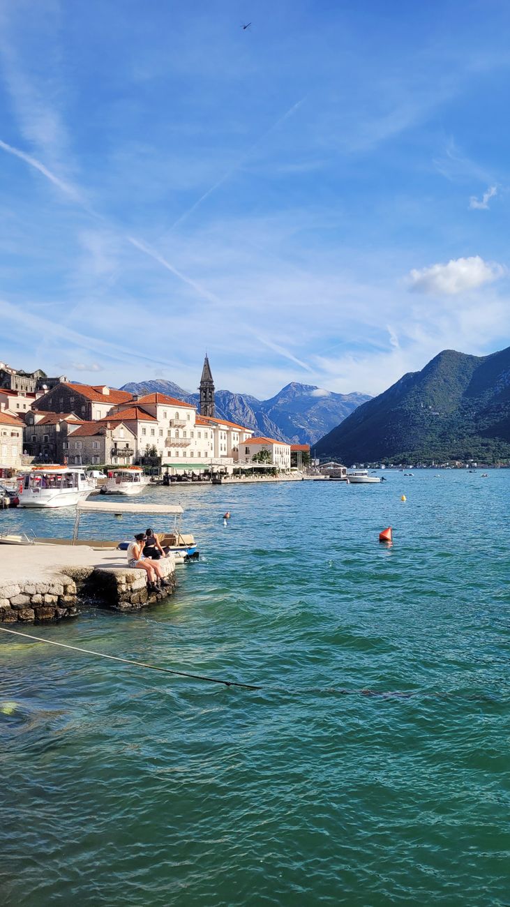 Picturesque view of a coastal town by the Adriatic Sea in the Bay of Kotor, with mountains and clear sky.