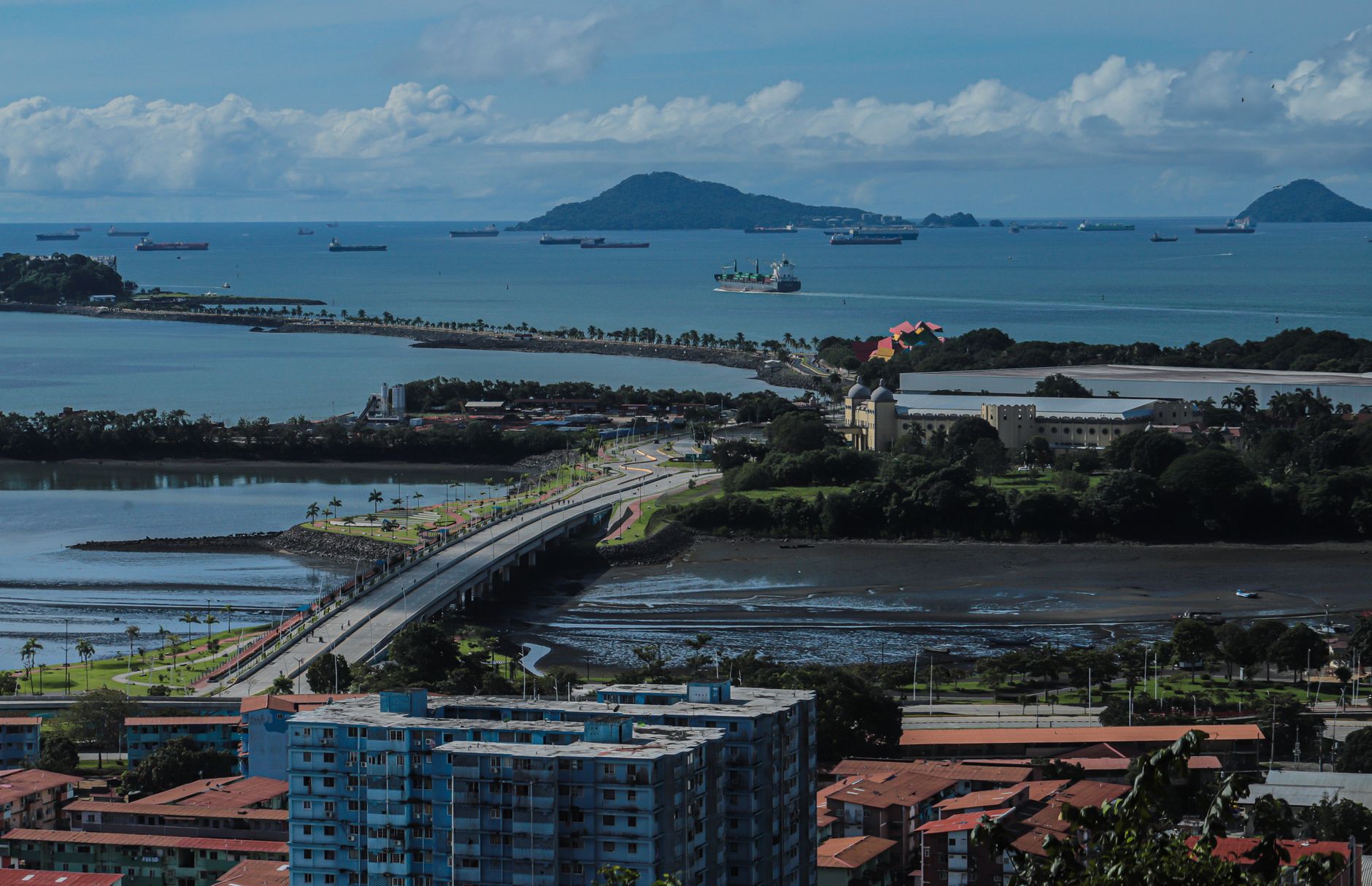 Aerial view of ships in Panamá Bay, featuring lush islands and urban landscape under a clear sky.