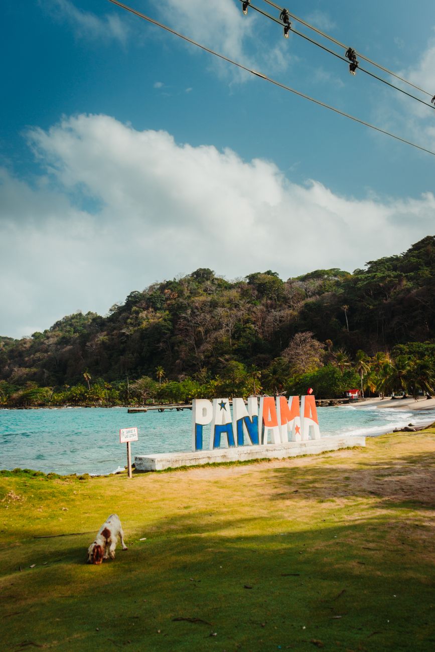 Panama beach with iconic sign, lush greenery, and clear blue sea under a bright sky.