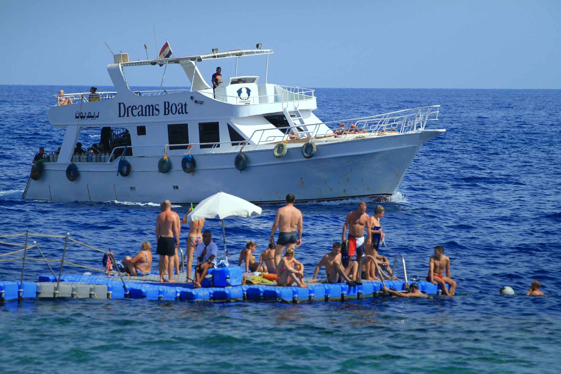 People relaxing on a sunny floating platform beside a boat on calm waters, evoking the unhurried leisure of a sea day onboard a vessel.