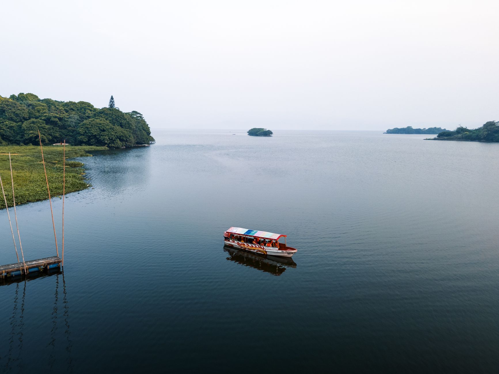 Aerial view of a boat traversing a tranquil green lake surrounded by lush tropical forest, evoking the experience of crossing Gatun Lake during a Panama Canal transit.