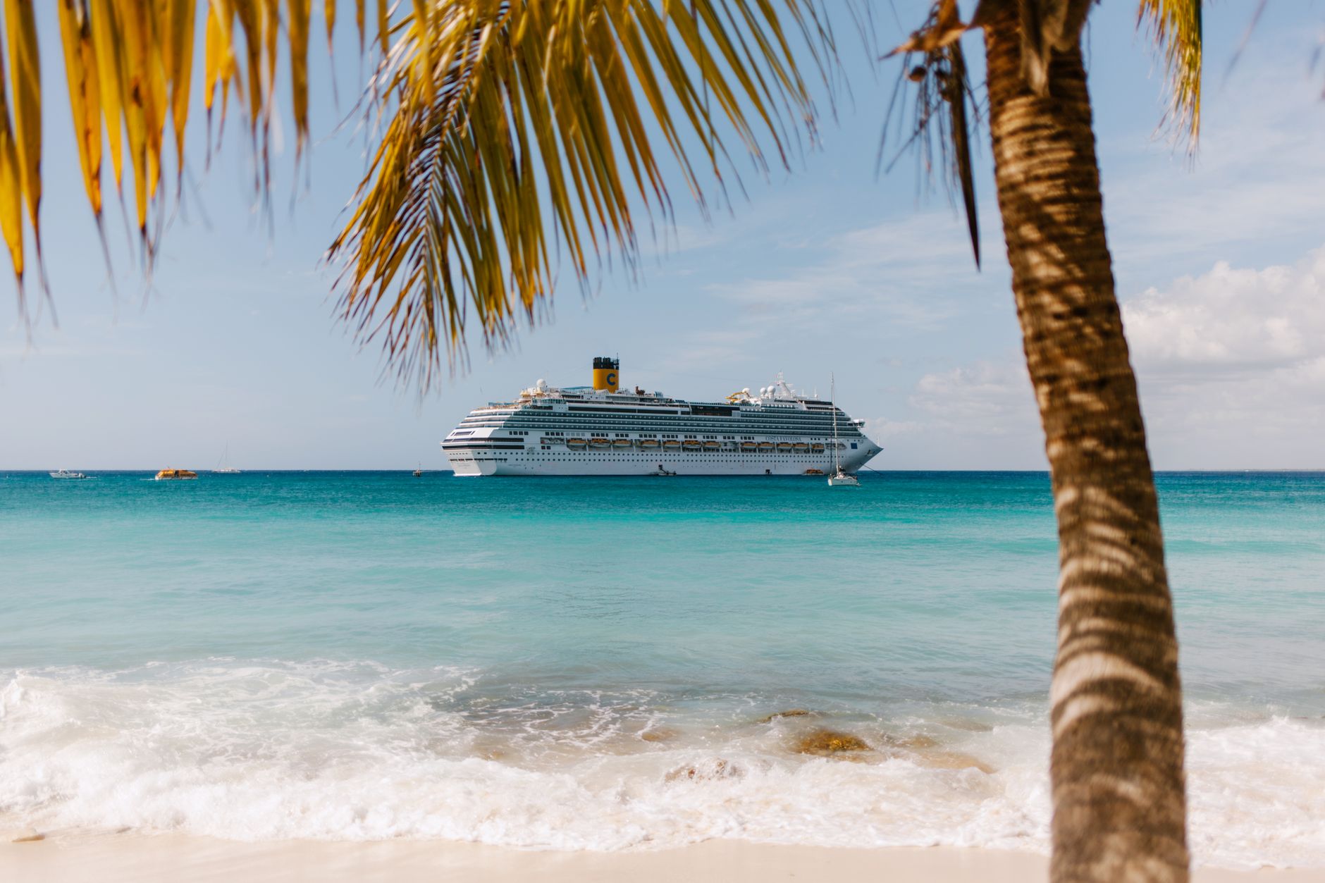A cruise ship sailing through turquoise Caribbean waters as seen from a tropical shoreline with a palm tree, evoking the southbound route toward the canal.