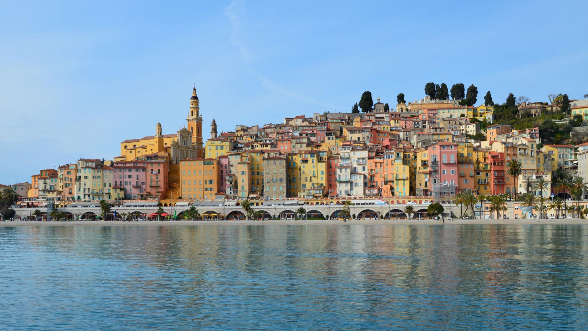 Colorful waterfront buildings of Menton lining the sparkling French Riviera coastline, showcasing the region's signature Mediterranean charm and azure waters.
