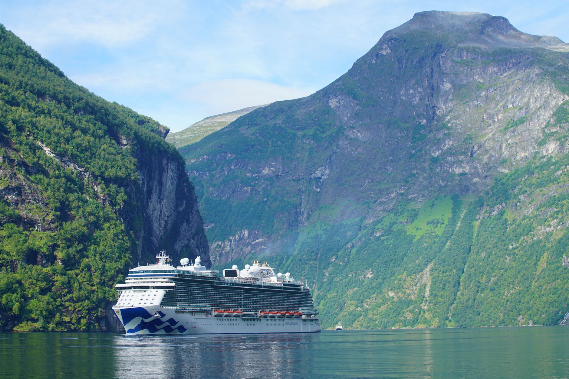 A cruise ship sailing through Norway's Geiranger Fjord, flanked by towering green mountains — a signature port of call on Europe cruises departing from Copenhagen.