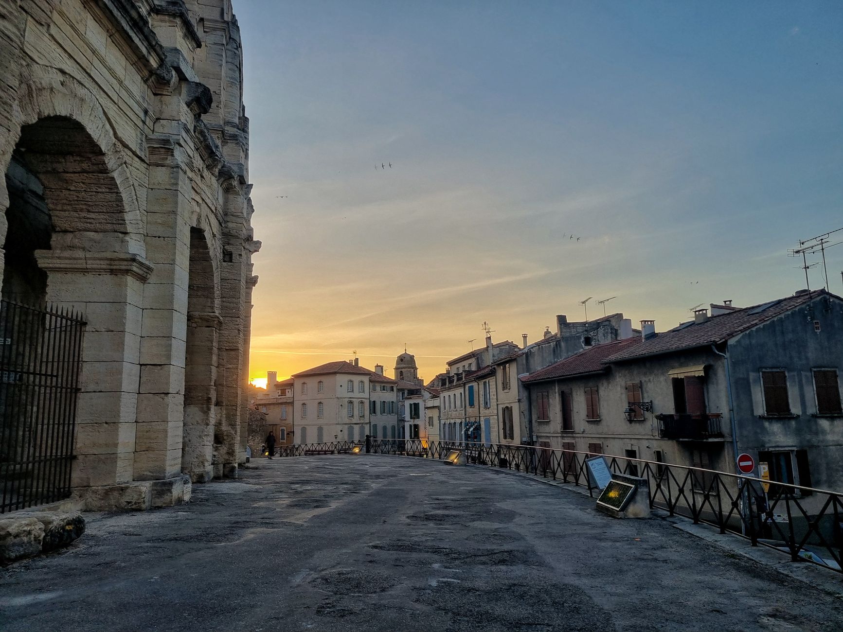The historic Arles Amphitheatre in Provence, France, glowing under warm sunset light that highlights its ancient Roman stone arches and architectural grandeur.