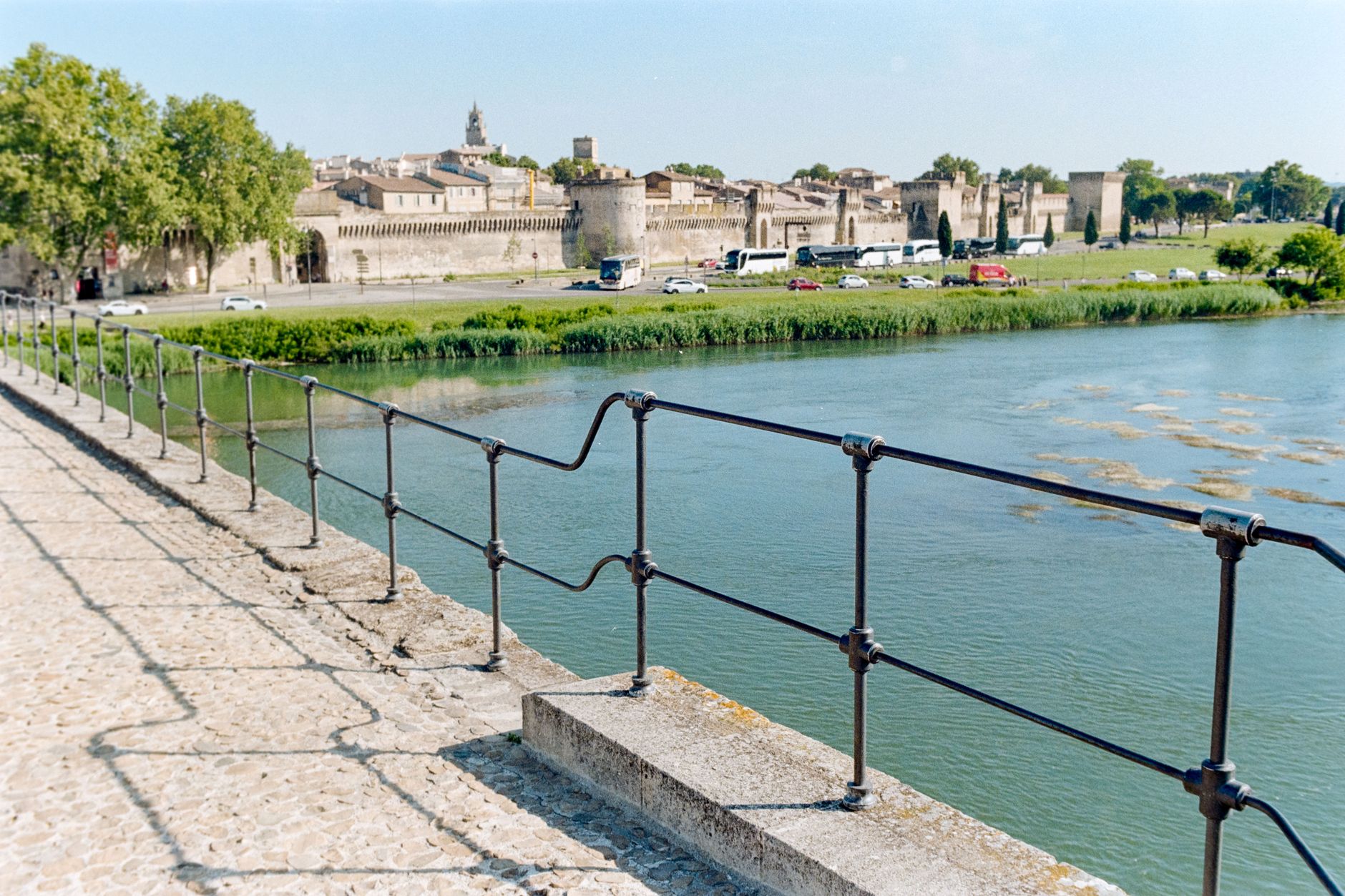 The historic medieval town walls of Avignon rising above the Rhône River, viewed from across the water, capturing the fortified stone ramparts that cruise passengers see as they sail along the river through Provence.