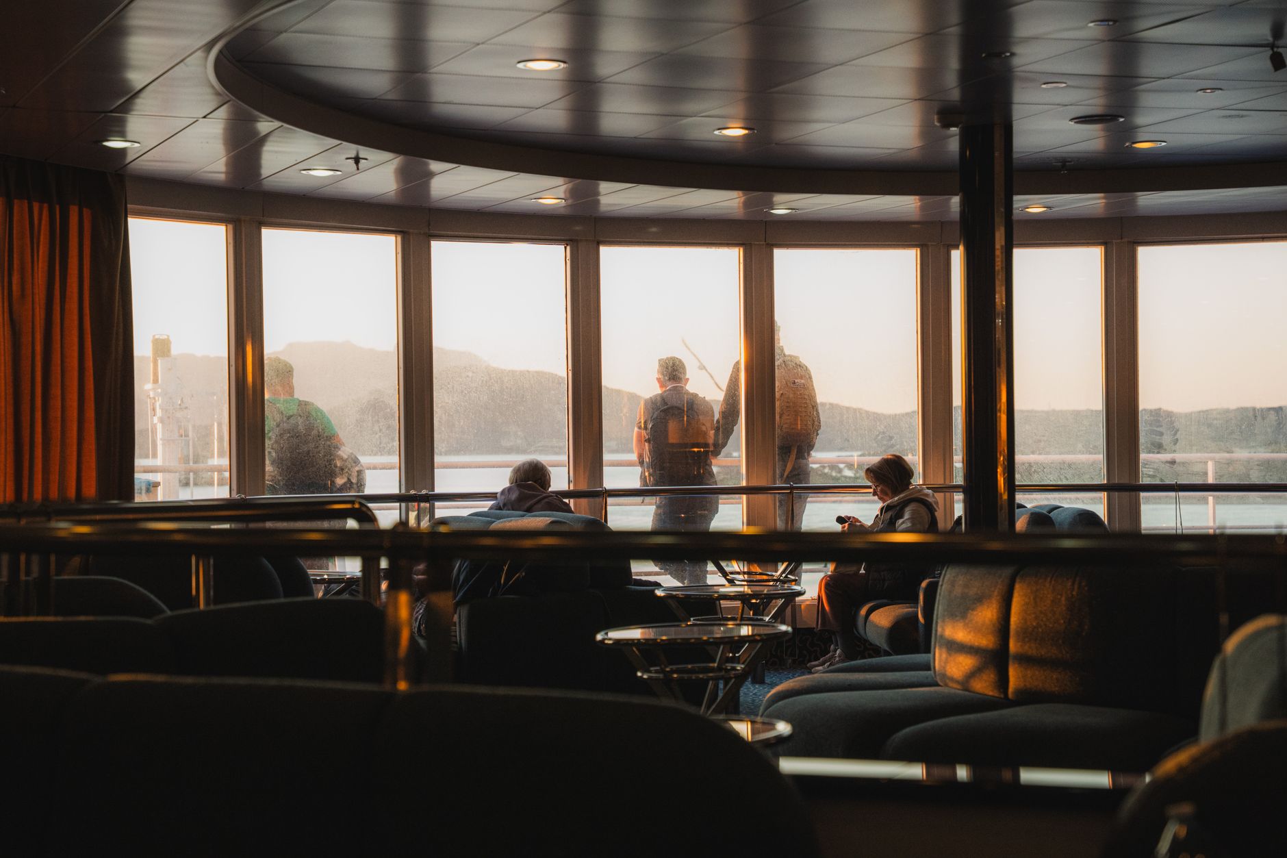 Passengers relaxing in an indoor lounge area with panoramic windows showcasing scenic views, evoking the intimate onboard atmosphere of a European river cruise sailing from Arles.