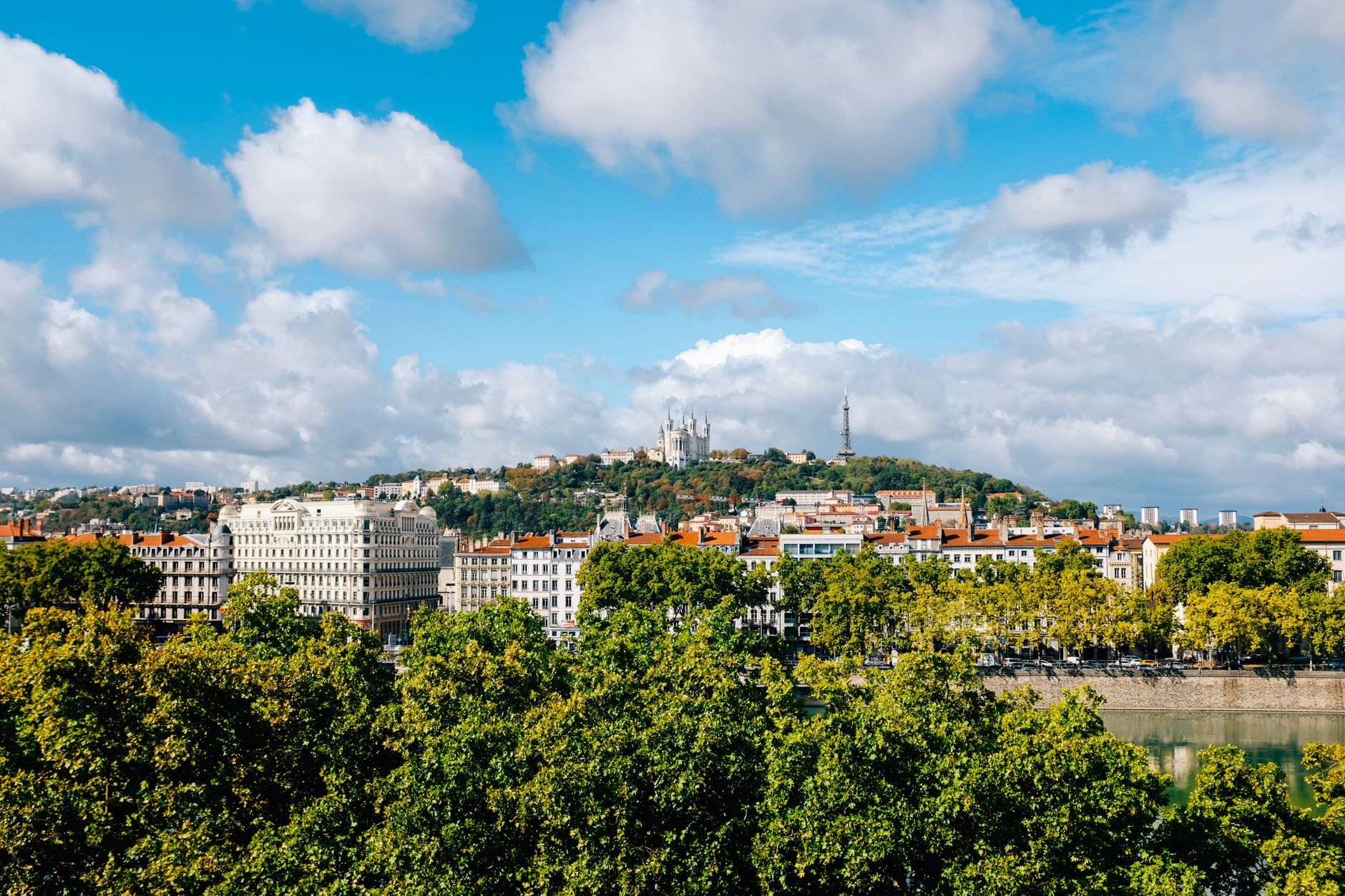 A riverside town along a French river valley with lush green hillsides, evoking the scenic Rhône corridor near Tournon-sur-Rhône