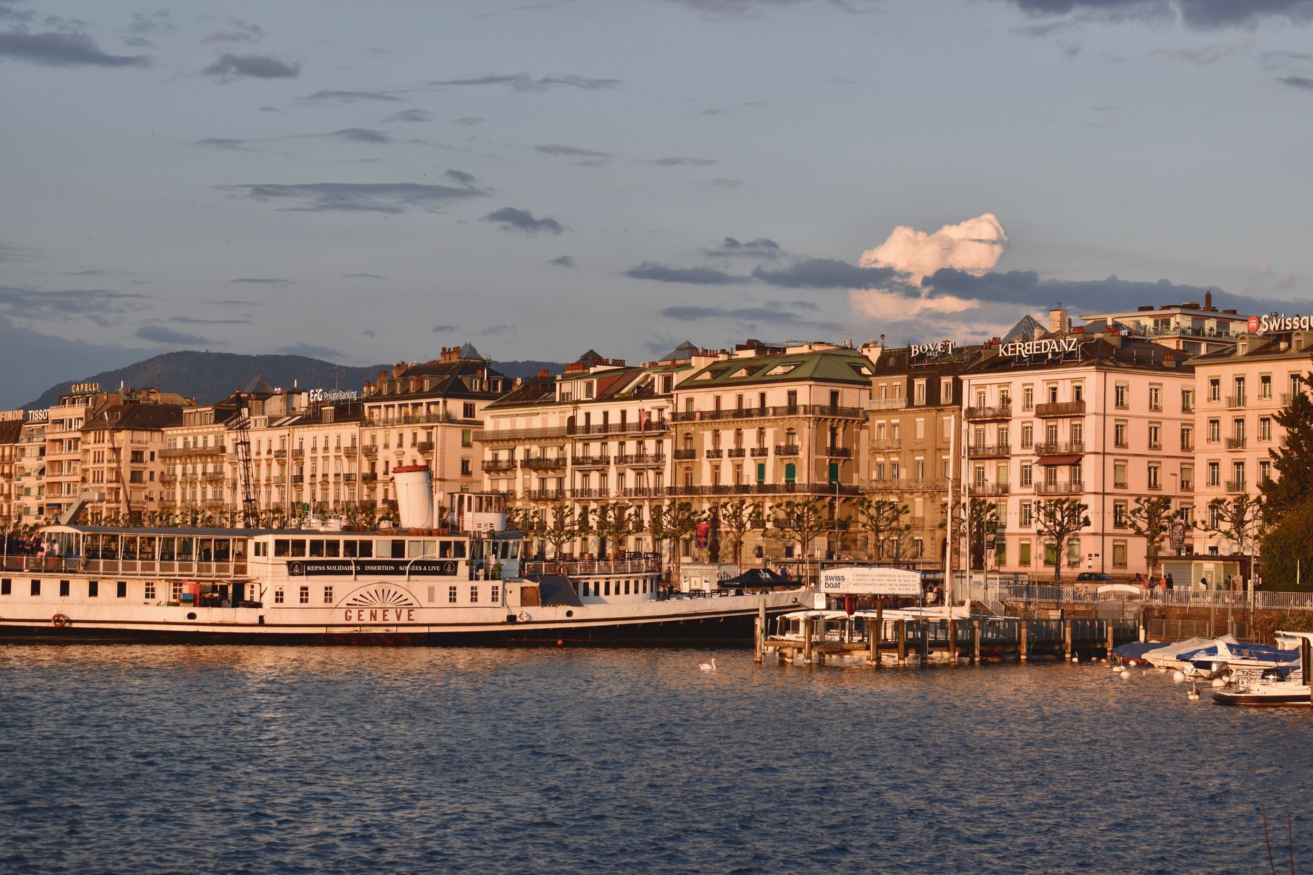 Geneva's historic waterfront architecture reflected along the lakeside at sunset, showcasing the charm of a European cruise departure point on Lake Geneva.