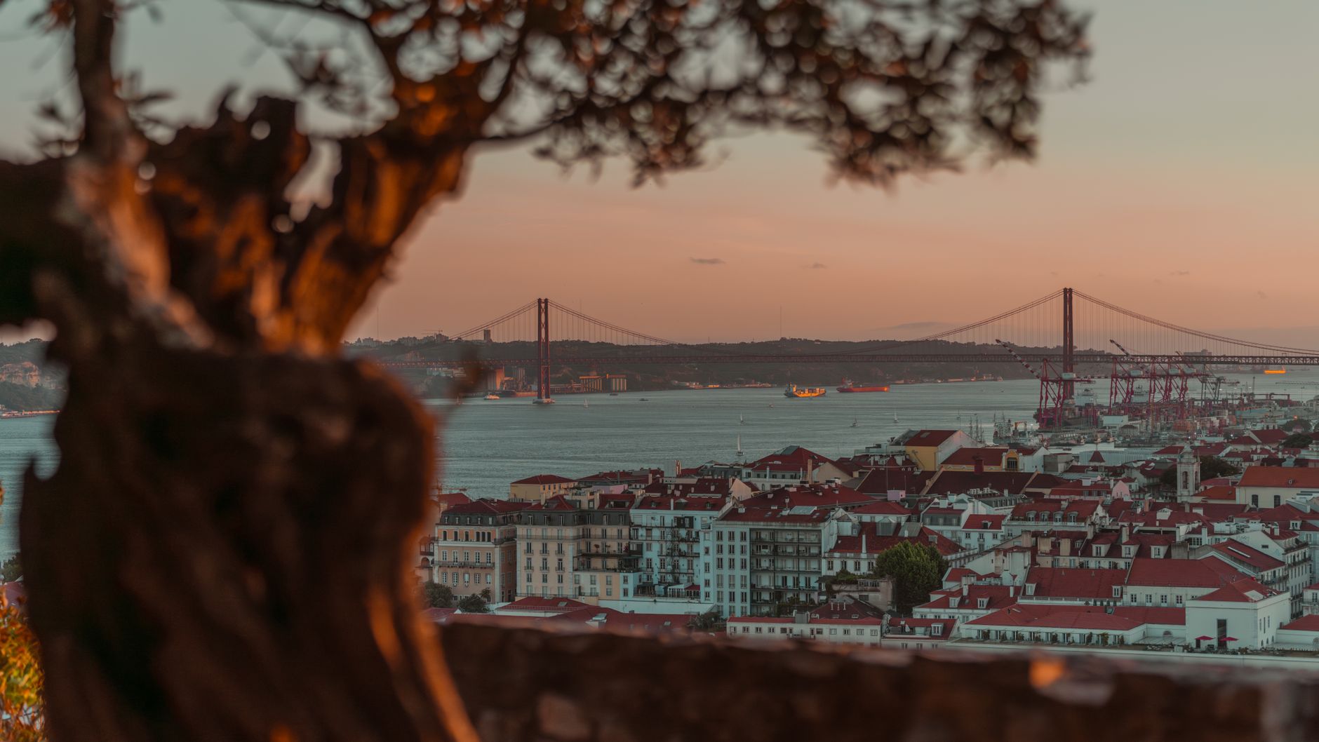 Sunset over Lisbon's skyline with the 25 de Abril Bridge spanning the Tagus River, evoking the departure point for European cruise itineraries from Portugal's capital.