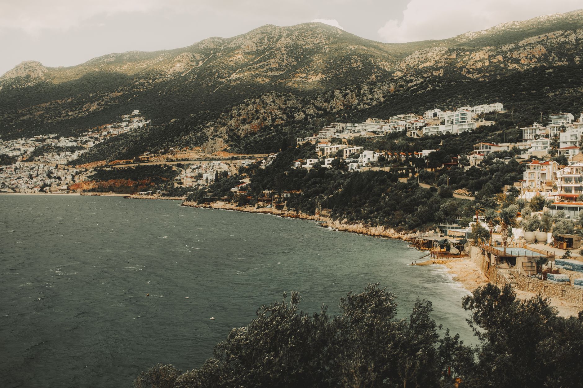 A picturesque Mediterranean coastal town with buildings nestled against a mountain backdrop, capturing the charm of a European cruise port along the Barcelona route.