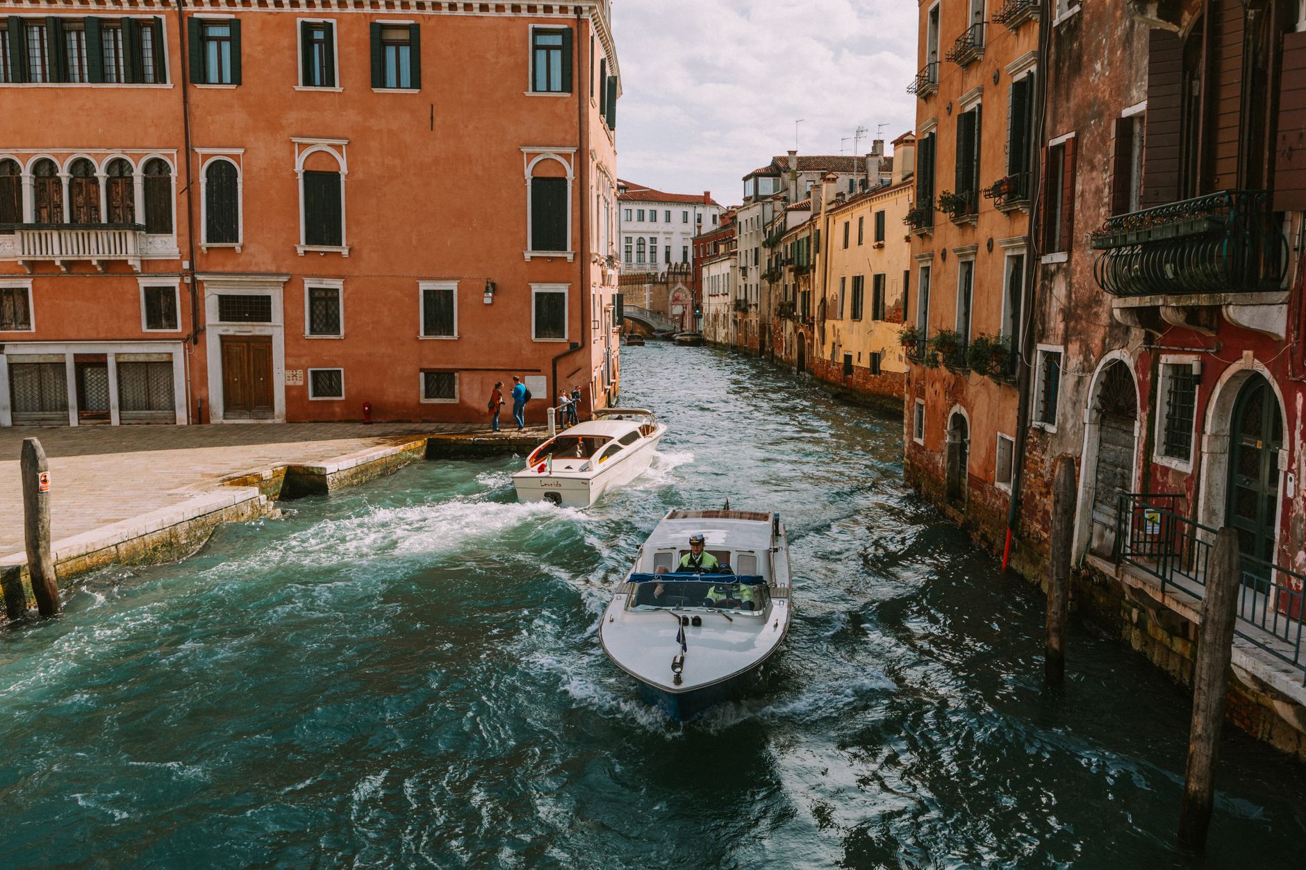 Boats navigating a picturesque canal among historic Venetian buildings on a sunny day.