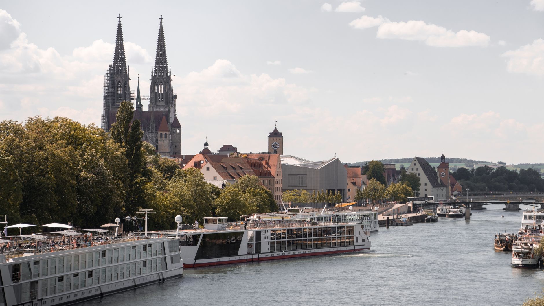 Regensburg's medieval skyline featuring St. Peter's Cathedral spires rising above the historic waterfront, with river cruise ships moored along the Danube River