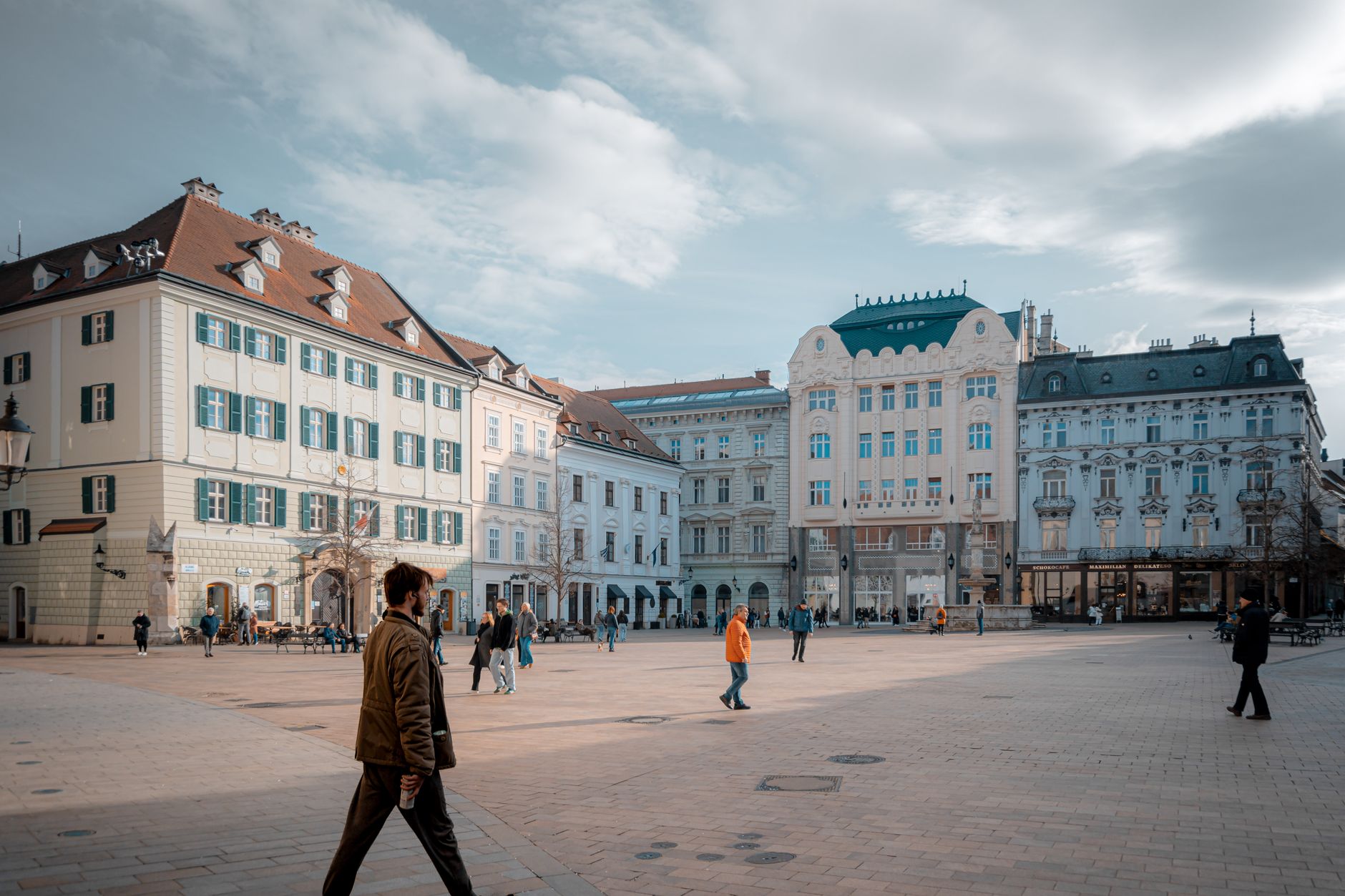 Pedestrians strolling through Bratislava's historic old town square lined with ornate facades, capturing the leisurely cultural exploration that defines a Danube river cruise port of call.
