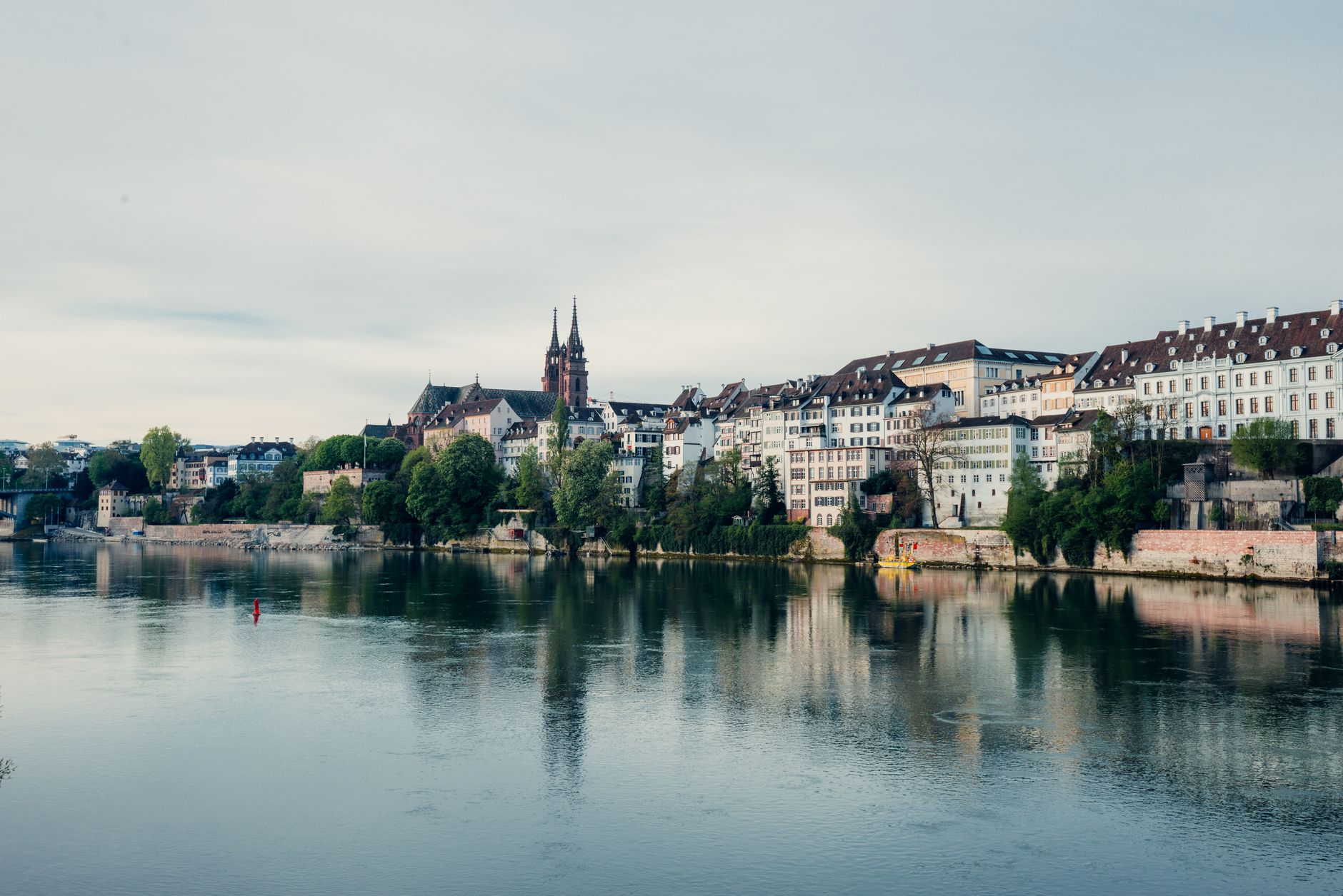 Historic old-town buildings and colourful facades lining Basel's Rhine riverfront, the embarkation point for cruises marketed as departing 'from Zurich'
