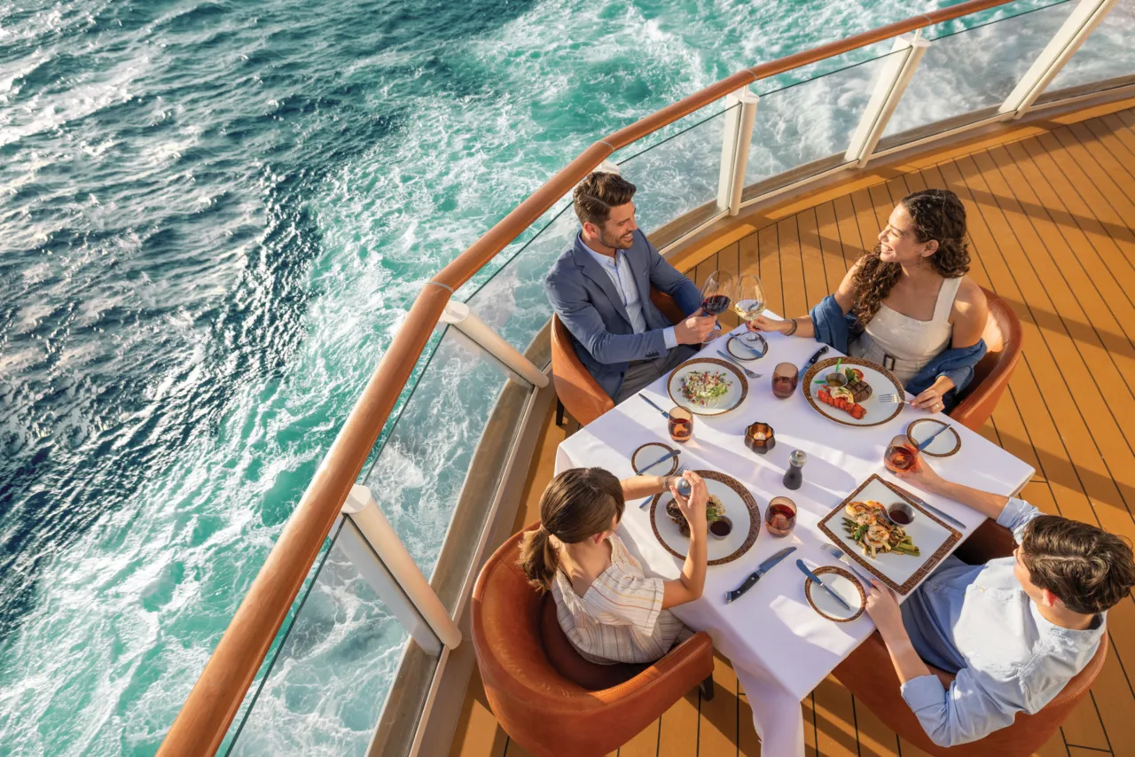 Elegant NCL Encore waterfront dining room with floor-to-ceiling ocean views and warm evening ambiance.