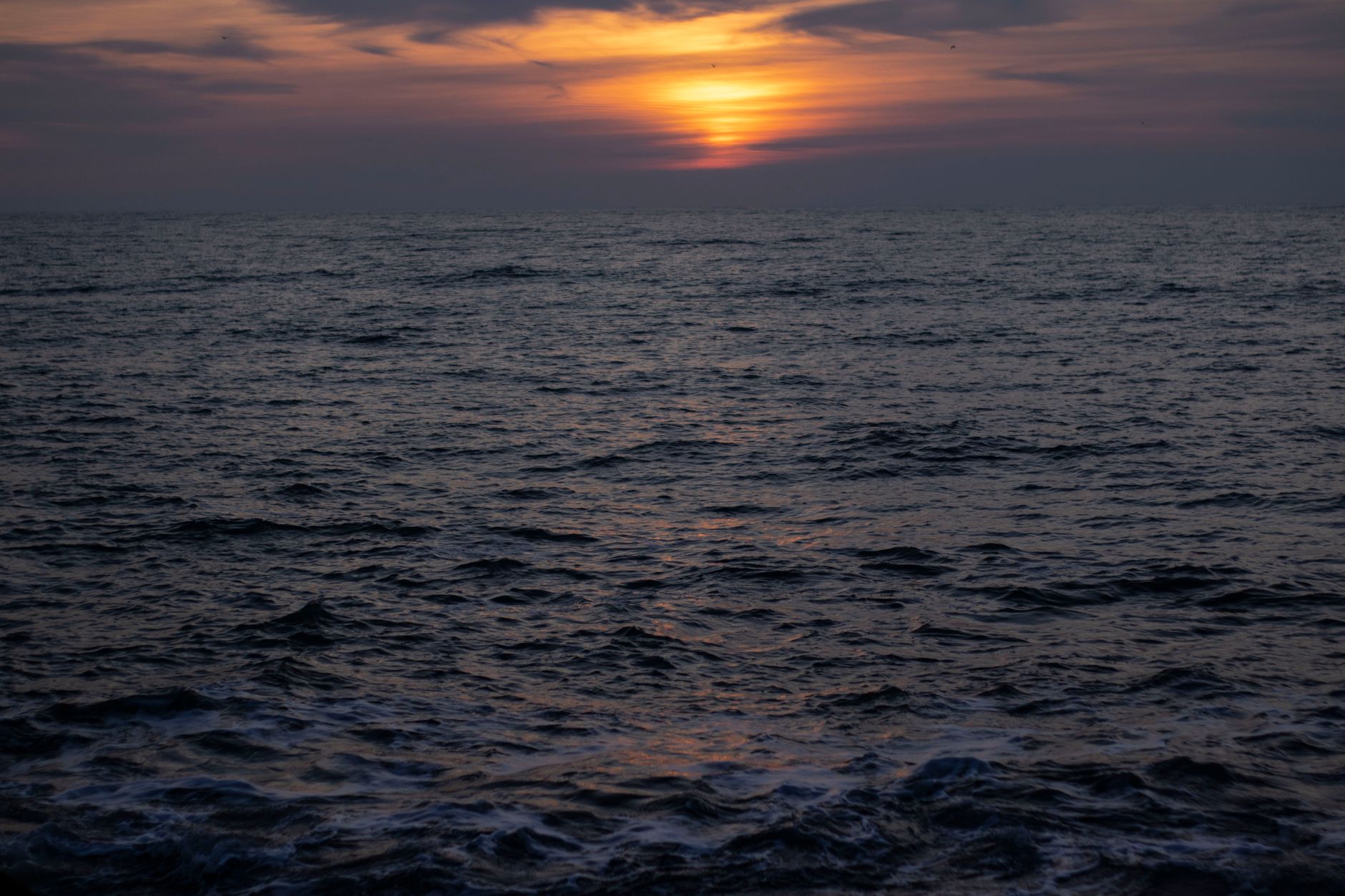 The sun descends toward the horizon over the vast Atlantic Ocean, casting warm golden light across the open water in a serene transatlantic seascape.