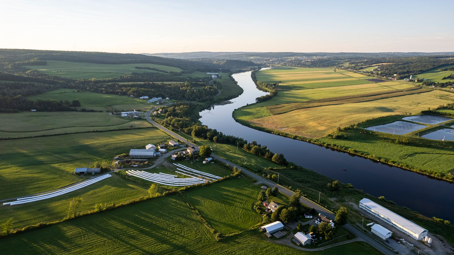 Aerial drone view of Quebec farmland along a winding river at sunset, capturing the gentle curves and expansive landscape of a Canadian river passage