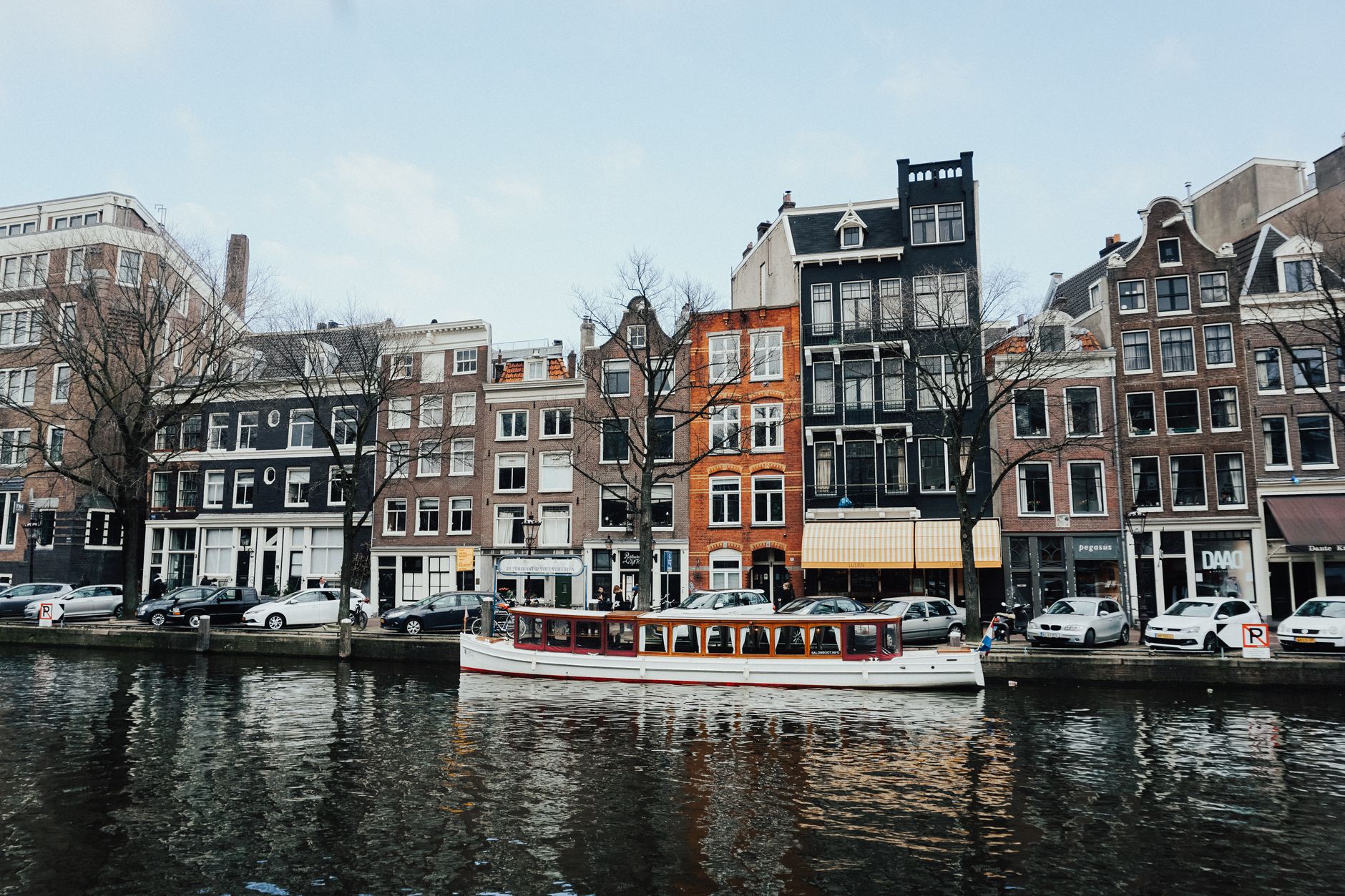 A boat cruises along an Amsterdam canal lined with classic Dutch architecture, setting the scene for European cruise departures from the city.