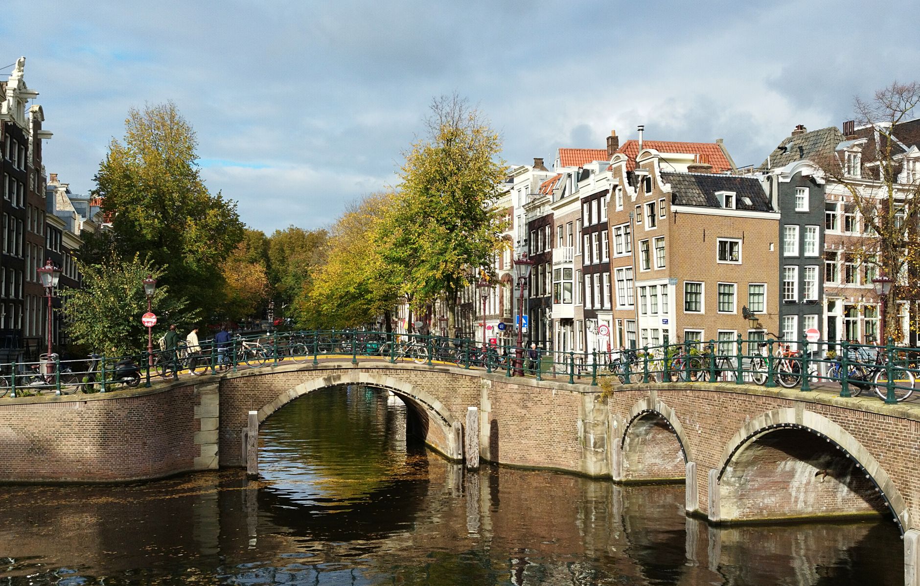 Scenic view of Amsterdam's iconic canal bridge with autumn foliage and historic buildings.