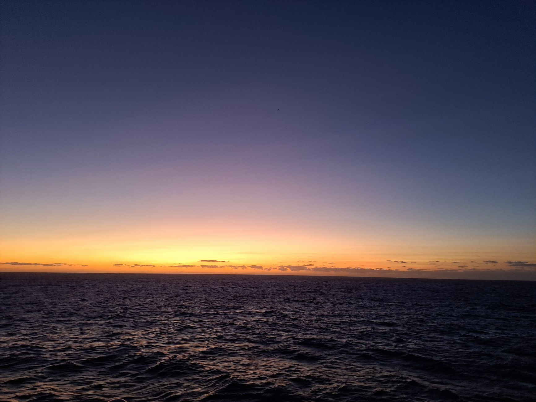 Vast open ocean at sunset with a vibrant gradient sky shifting from deep indigo waters to amber and pink hues along the endless Atlantic horizon
